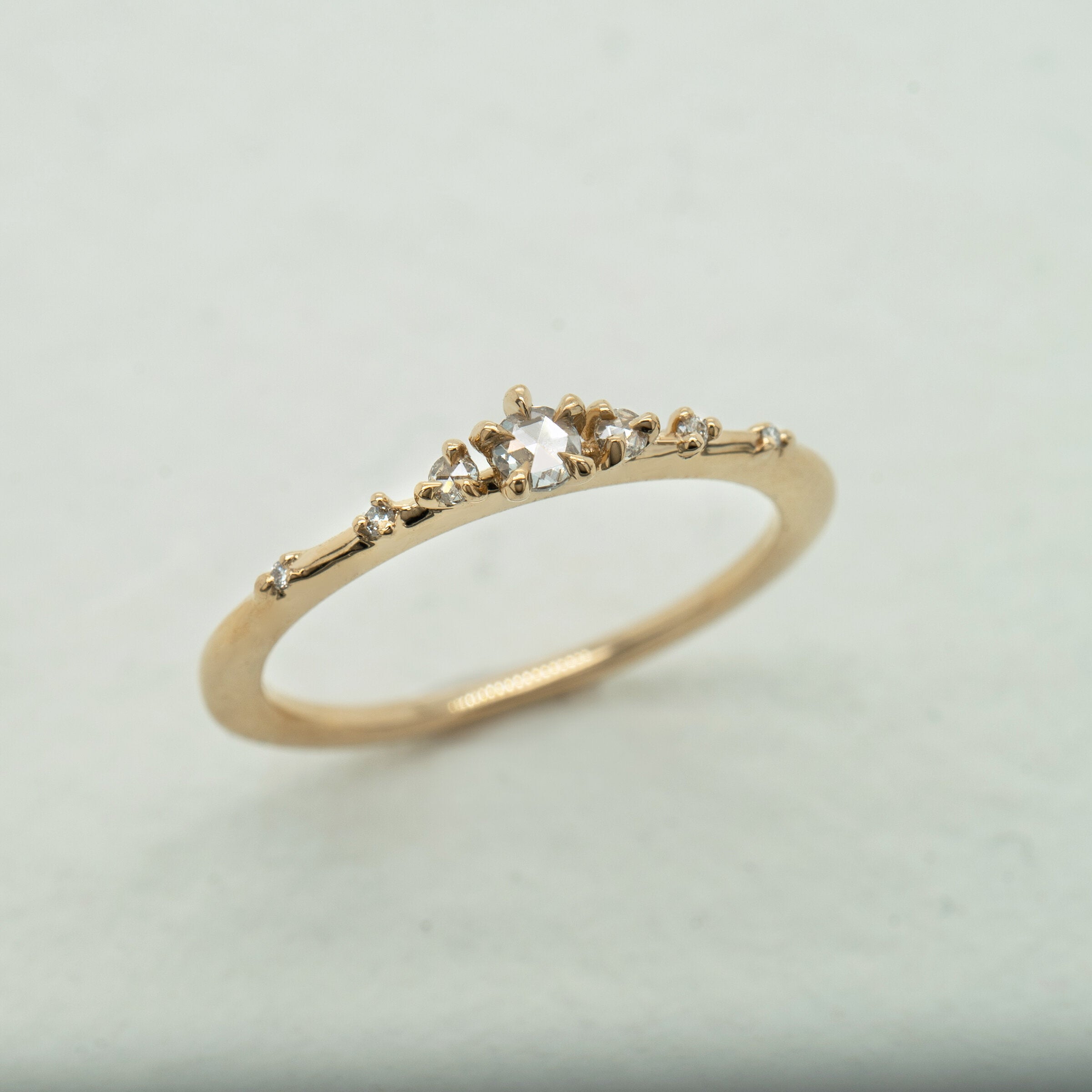 A product photo of Laurie Fleming Jewellery's "Water Lily Ring," a delicate solid gold stacking ring with round brilliant and rose cut diamonds scattered along the band. The ring is on a light grey background.