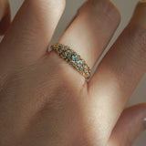 Laurie Fleming Jewellery's "Moss Signet Ring," a bold solid gold signet-style ring encrusted with varying shades and sizes of blue-green teal sapphires on the band. The ring is worn on a hand in front of a light grey background; most of the photo is in the shade, but a beam of light is shining perfectly across the ring.