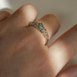 Laurie Fleming Jewellery's "Moss Signet Ring," a bold solid gold signet-style ring encrusted with varying shades and sizes of blue-green teal sapphires on the band. The ring is worn on a hand in front of a light grey background; most of the photo is in the shade, but a beam of light is shining perfectly across the ring.