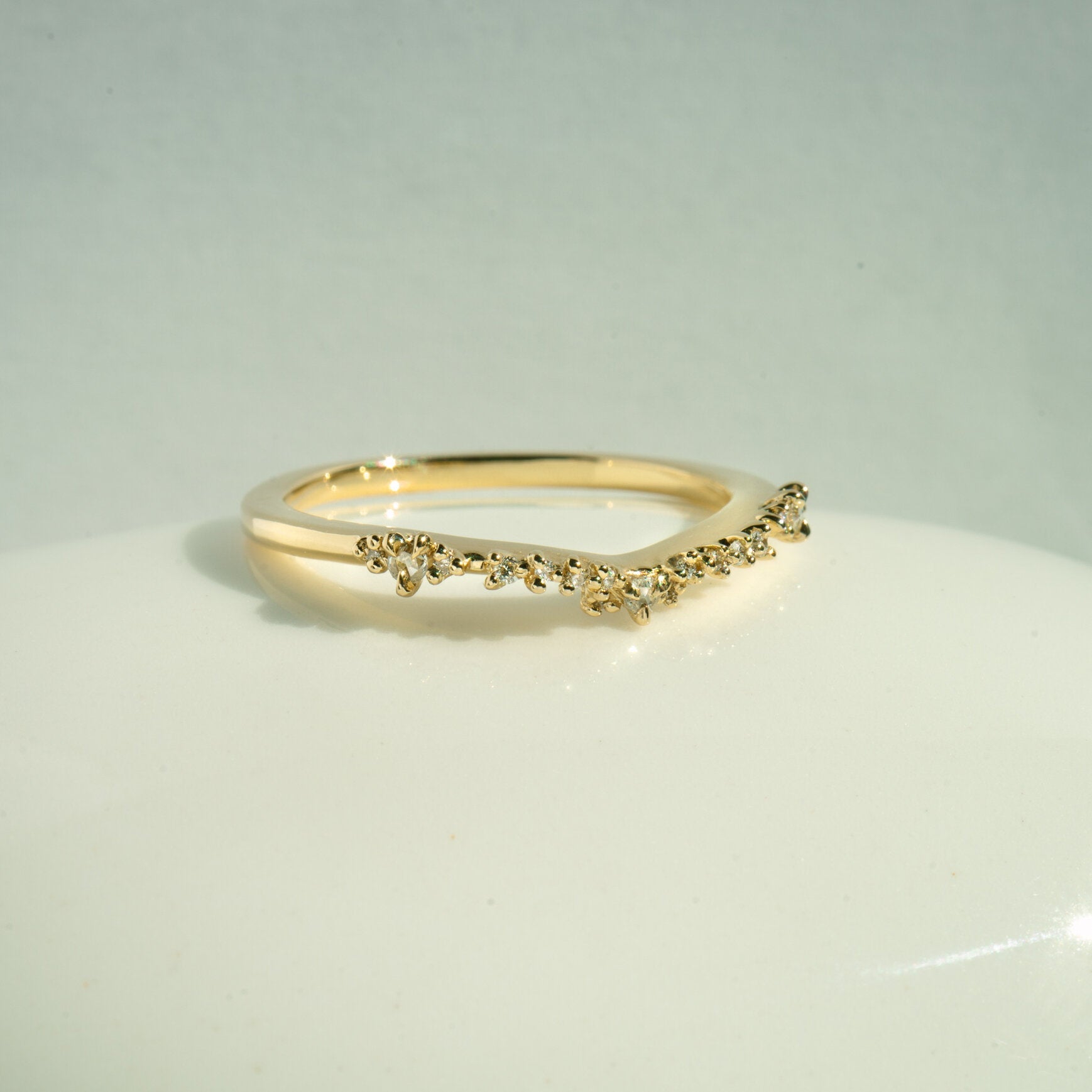 The Sylph Band ring by Laurie Fleming Jewellery, which features a subtly curved band to fit contour around another ring. The band features round brilliant and rose cut diamonds. It is resting against a white background.