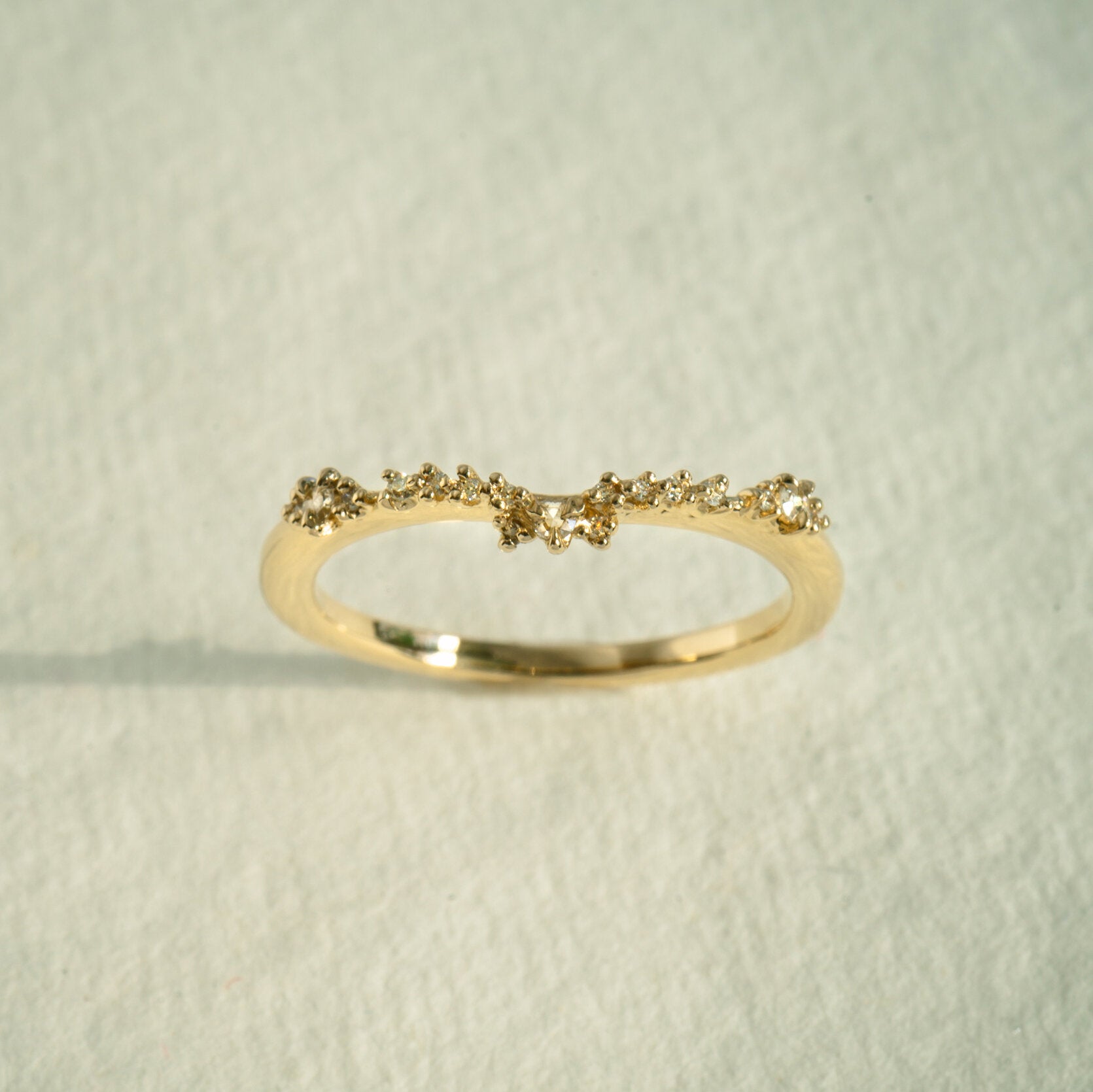 The Sylph Band ring by Laurie Fleming Jewellery, which features a subtly curved band to fit contour around another ring. The band features round brilliant and rose cut diamonds. It is resting against a white background.