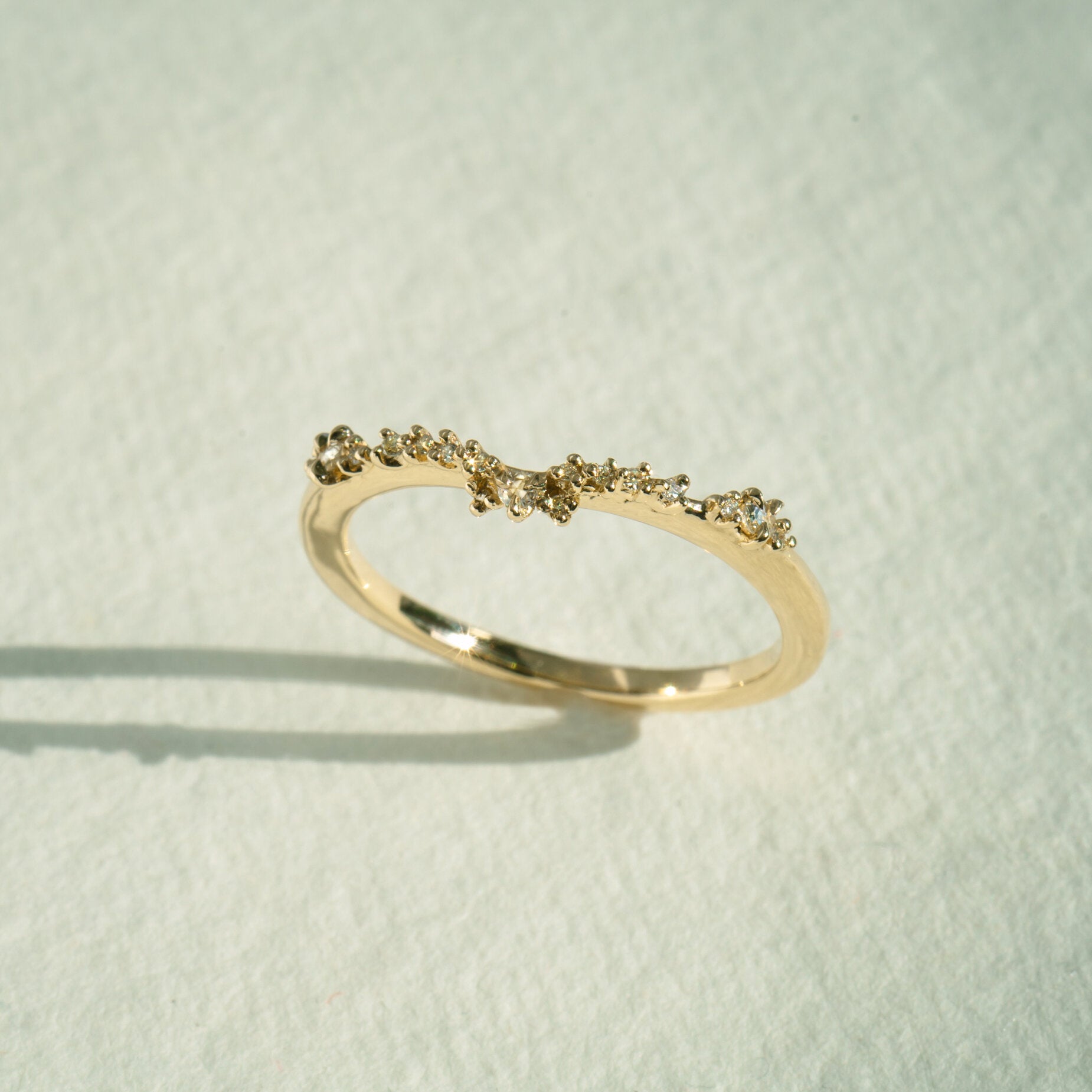The Sylph Band ring by Laurie Fleming Jewellery, which features a subtly curved band to fit contour around another ring. The band features round brilliant and rose cut diamonds. It is resting against a white background.