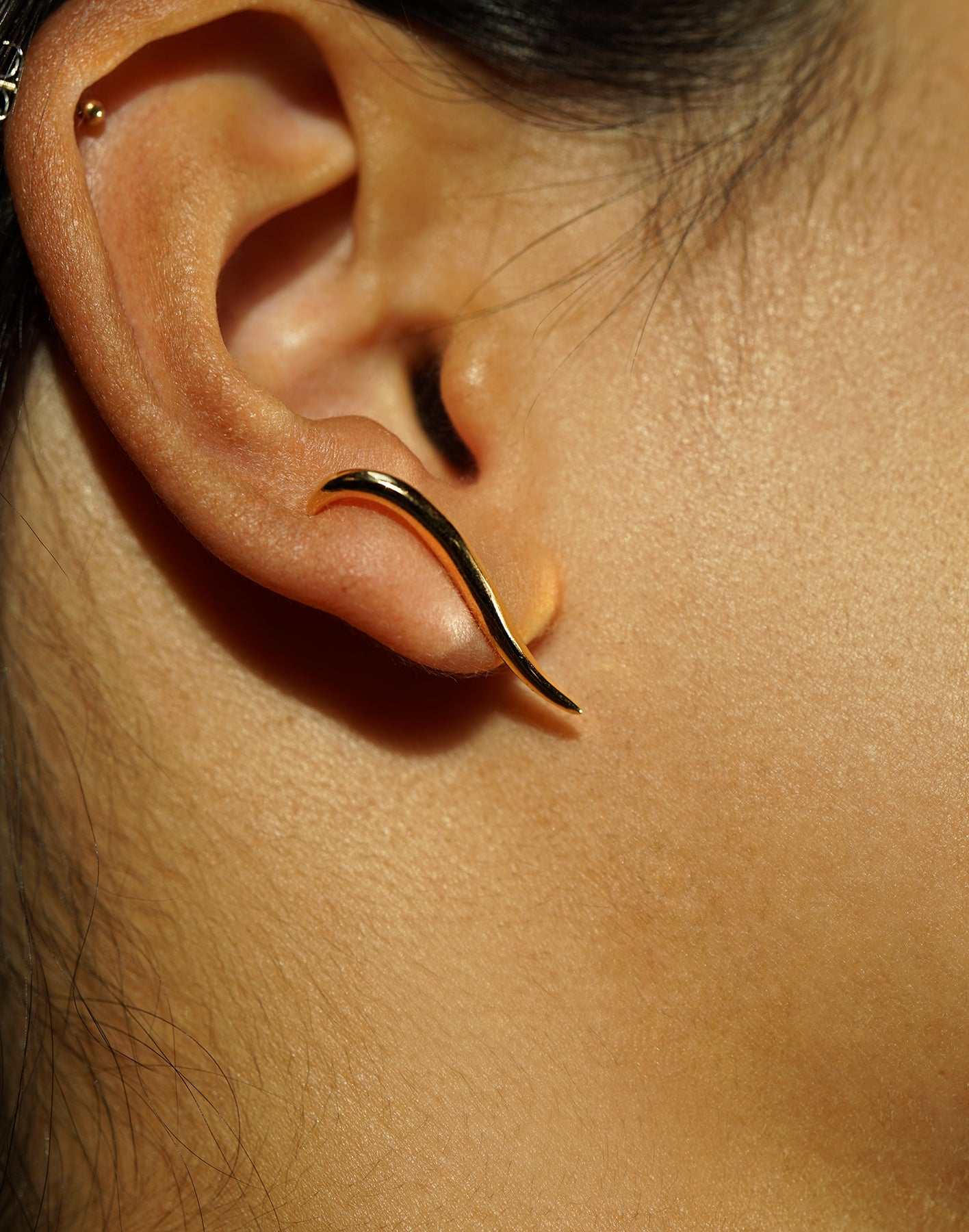 A close-up of an ear showing one of the possible ways to wear the hand-carved sculptural solid gold "Versare" earrings by Laurie Fleming Jewellery.