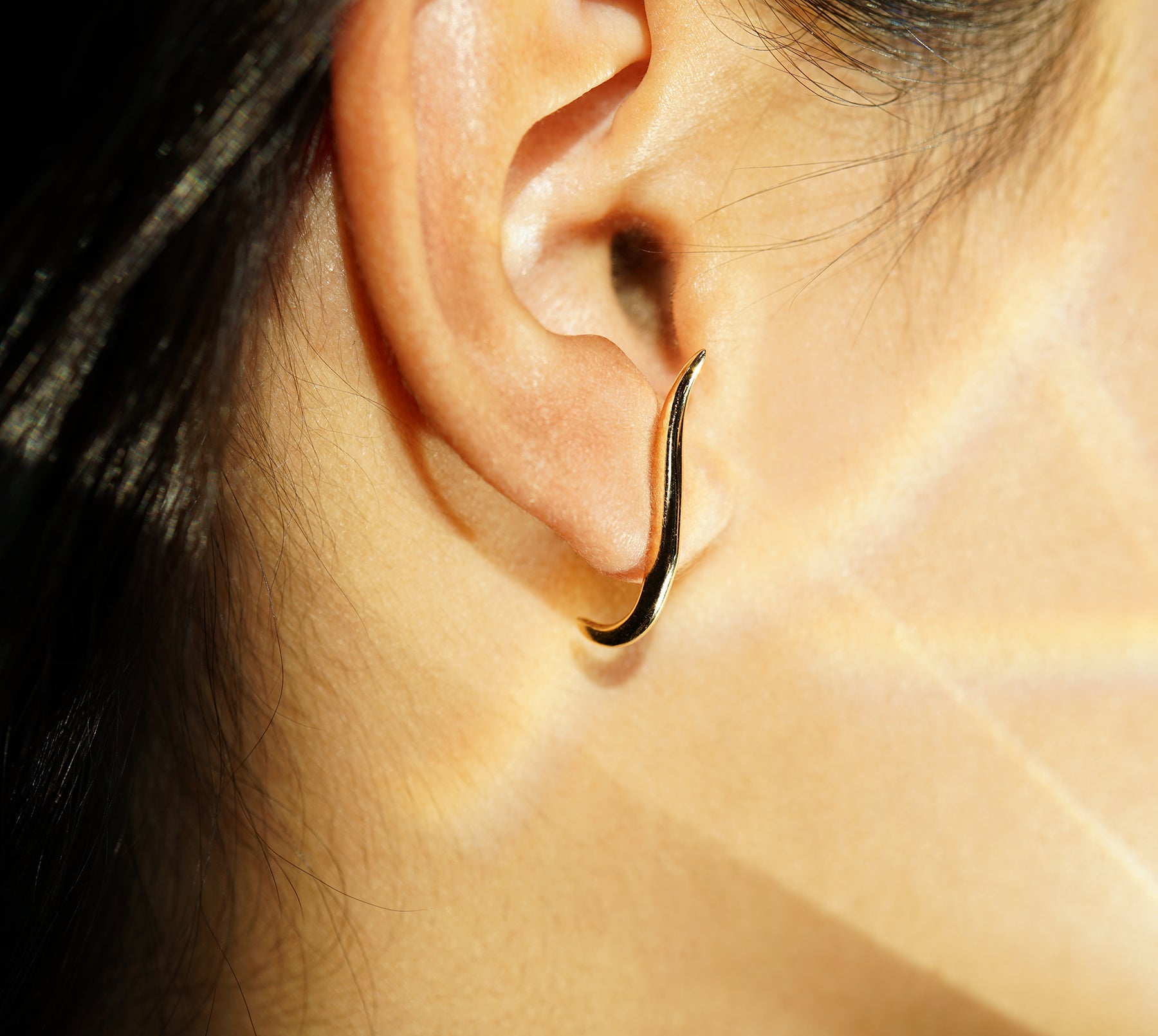 A close-up of an ear showing one of the possible ways to wear the hand-carved sculptural solid gold "Versare" earrings by Laurie Fleming Jewellery.