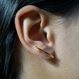 A close-up of an ear showing one of the possible ways to wear the hand-carved sculptural solid gold "Versare" earrings by Laurie Fleming Jewellery.