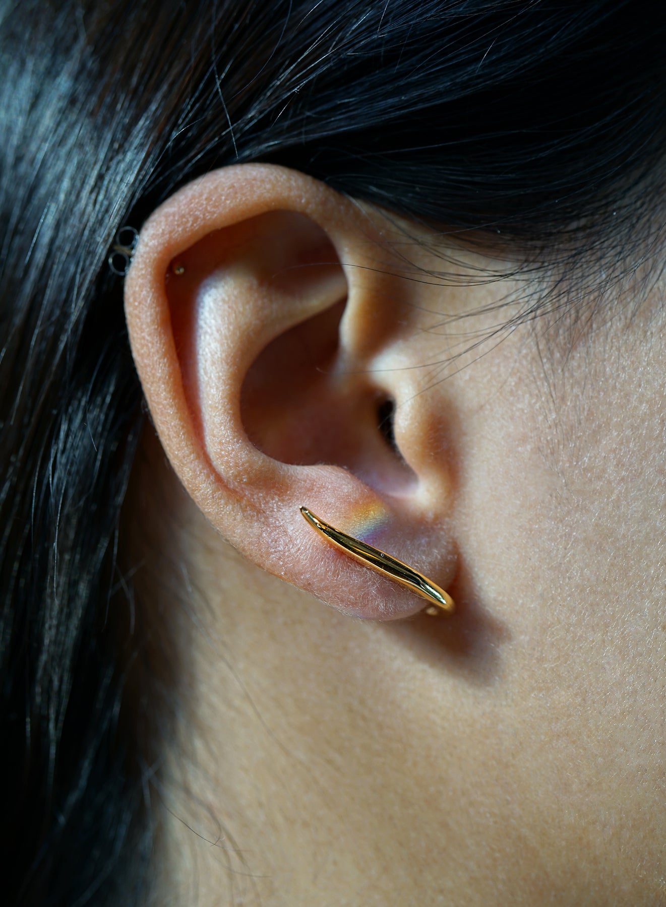 A close-up of an ear showing one of the possible ways to wear the hand-carved sculptural solid gold "Versare" earrings by Laurie Fleming Jewellery.